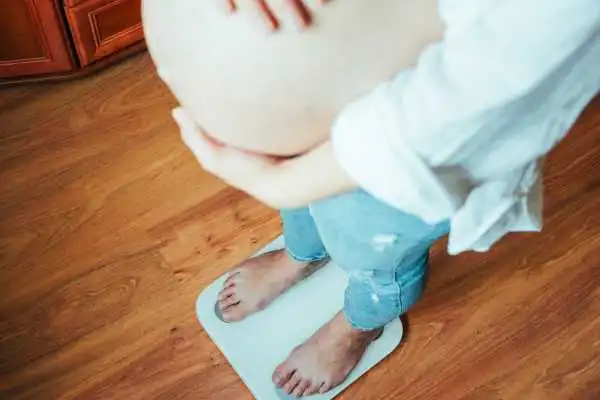 Image of woman weighing herself and experiencing weight gain through pregnancy Lowestoft
